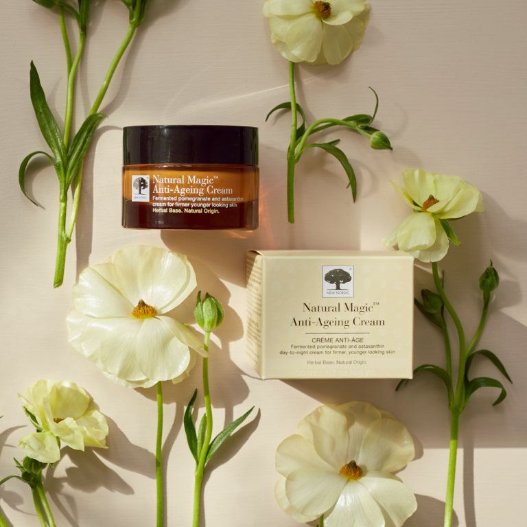 „Natural Magic™“ pretnovecošanās krēms, ko ieskauj svaigi ziedi.