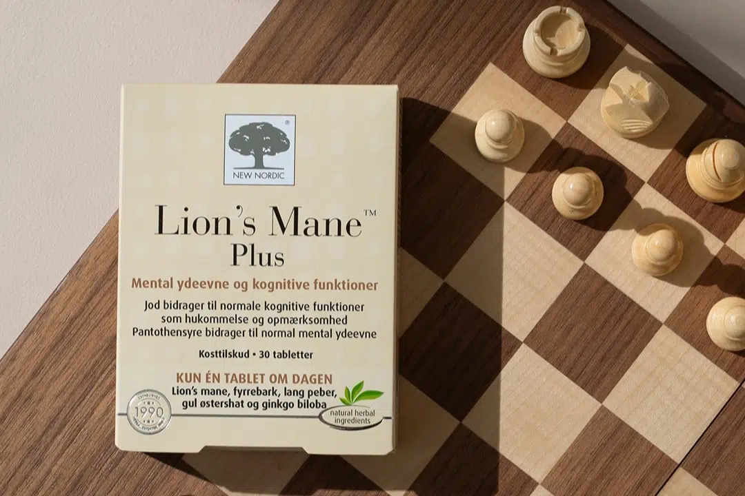 Lion’s Mane Plus iepakojums blakus šaha galdiņam un figūrām