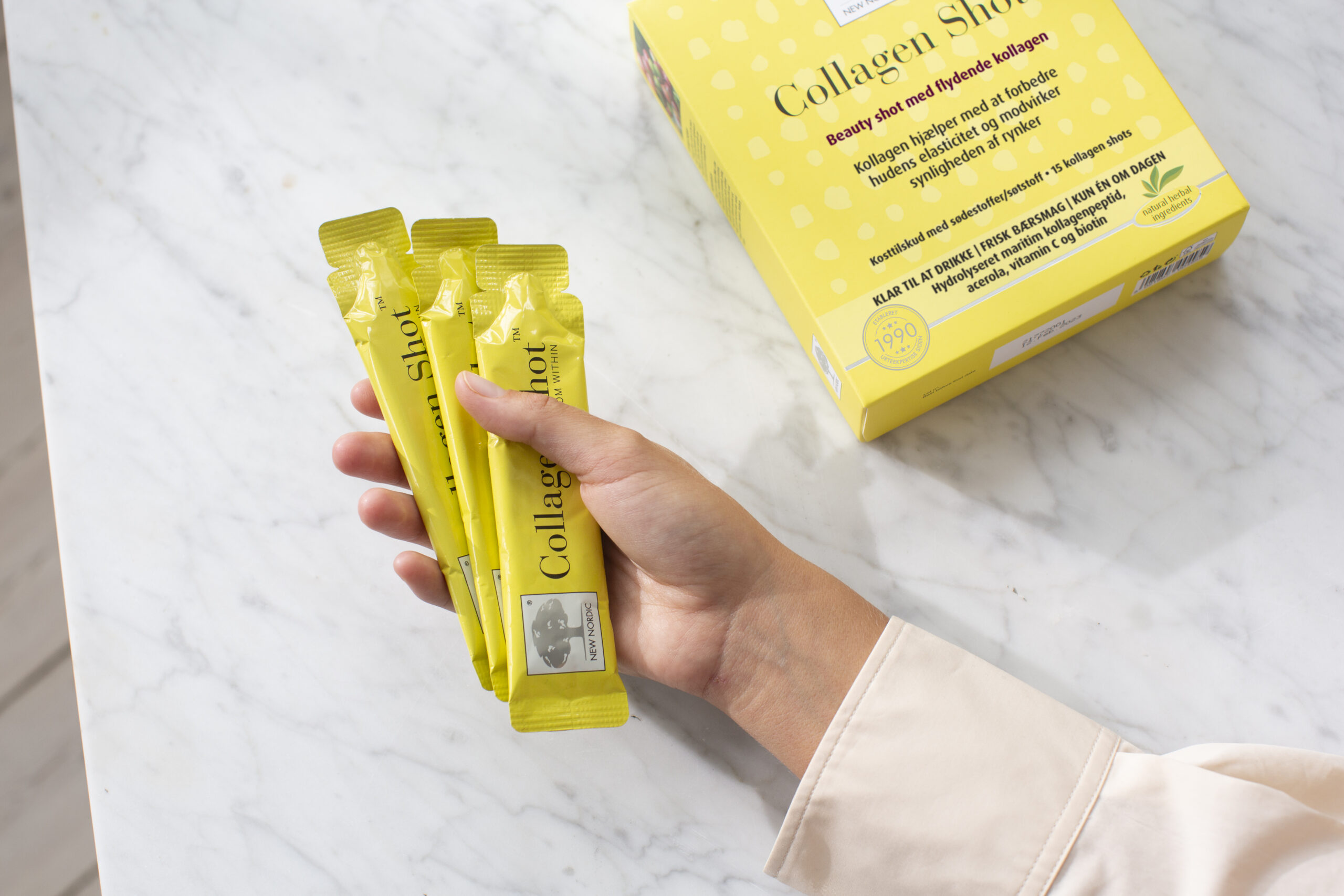 Collagen Shot paciņas ar produkta iepakojumu uz gaiša marmora fona