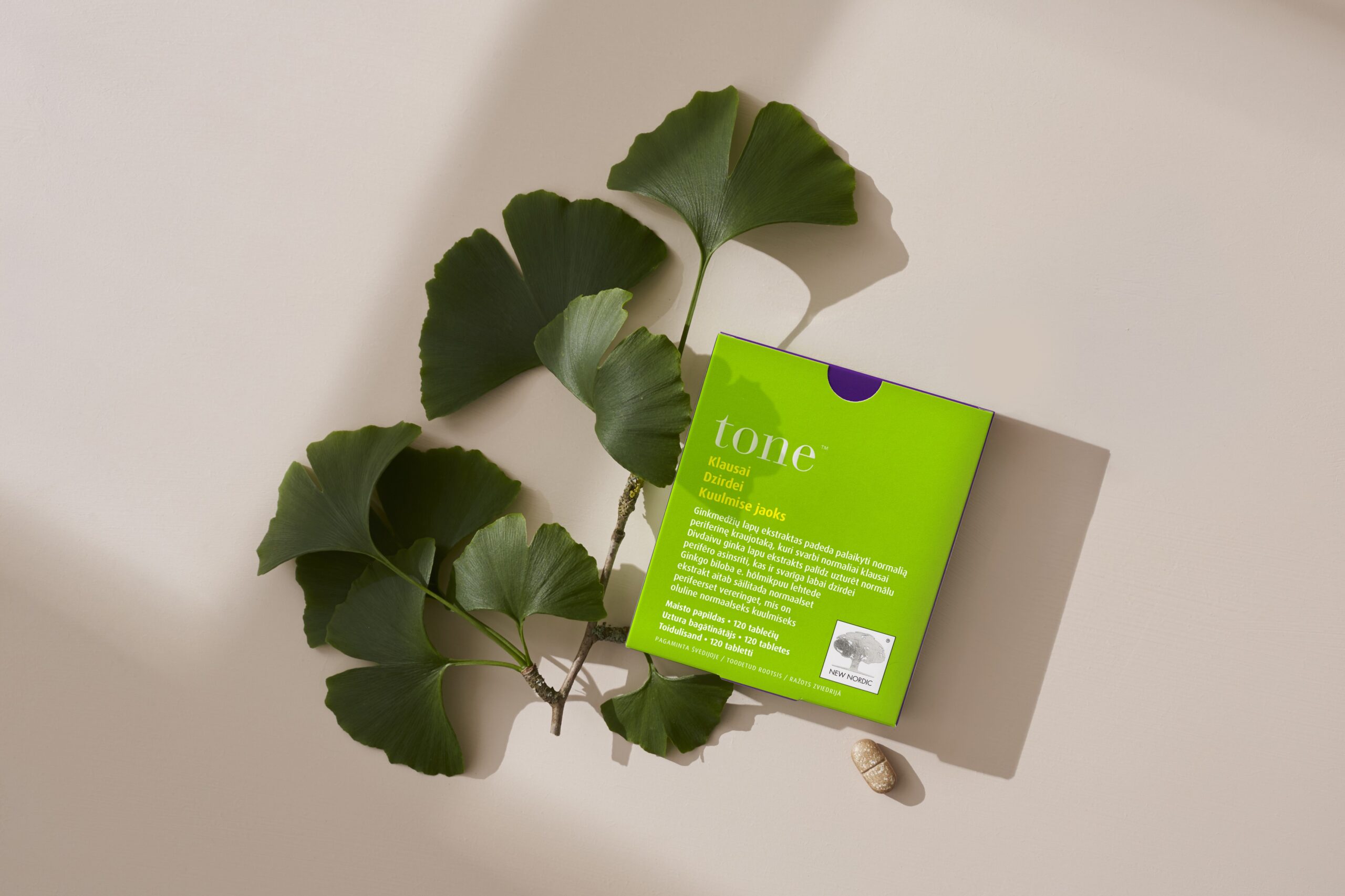 Ear Tone produkta iepakojums ar ginkgo lapām uz bēša fona
